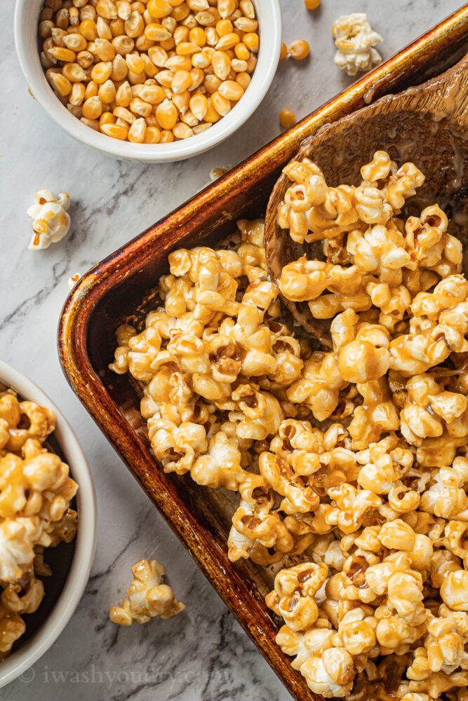 caramel corn in metal pan with spoon and popcorn kernels in white bowl 