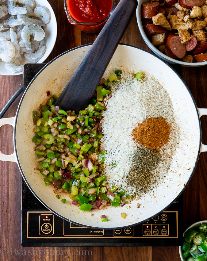 rice with seasonings in pan along with vegetables and wooden spoon