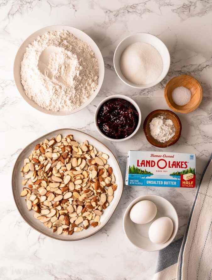 ingredients for thumbprint cookies on white table with almonds and raspberry jam