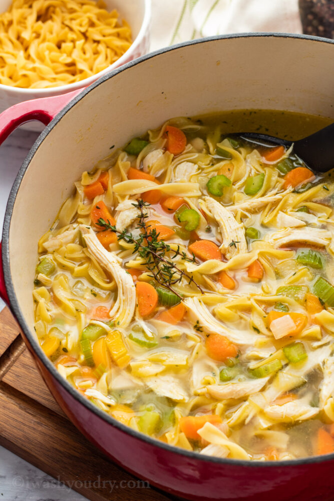 Cooked Chicken Noodle Soup in red pot on wood cutting board.