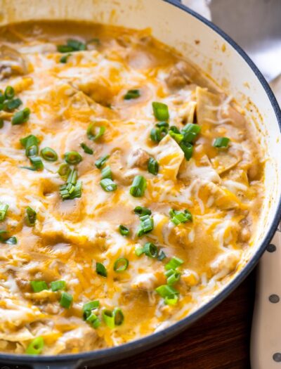 Skillet with cheesy chicken enchiladas and green onions