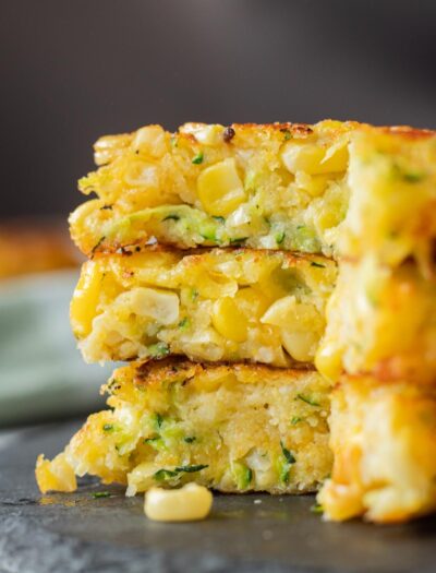 3 sliced zucchini corn fritters on black slate.