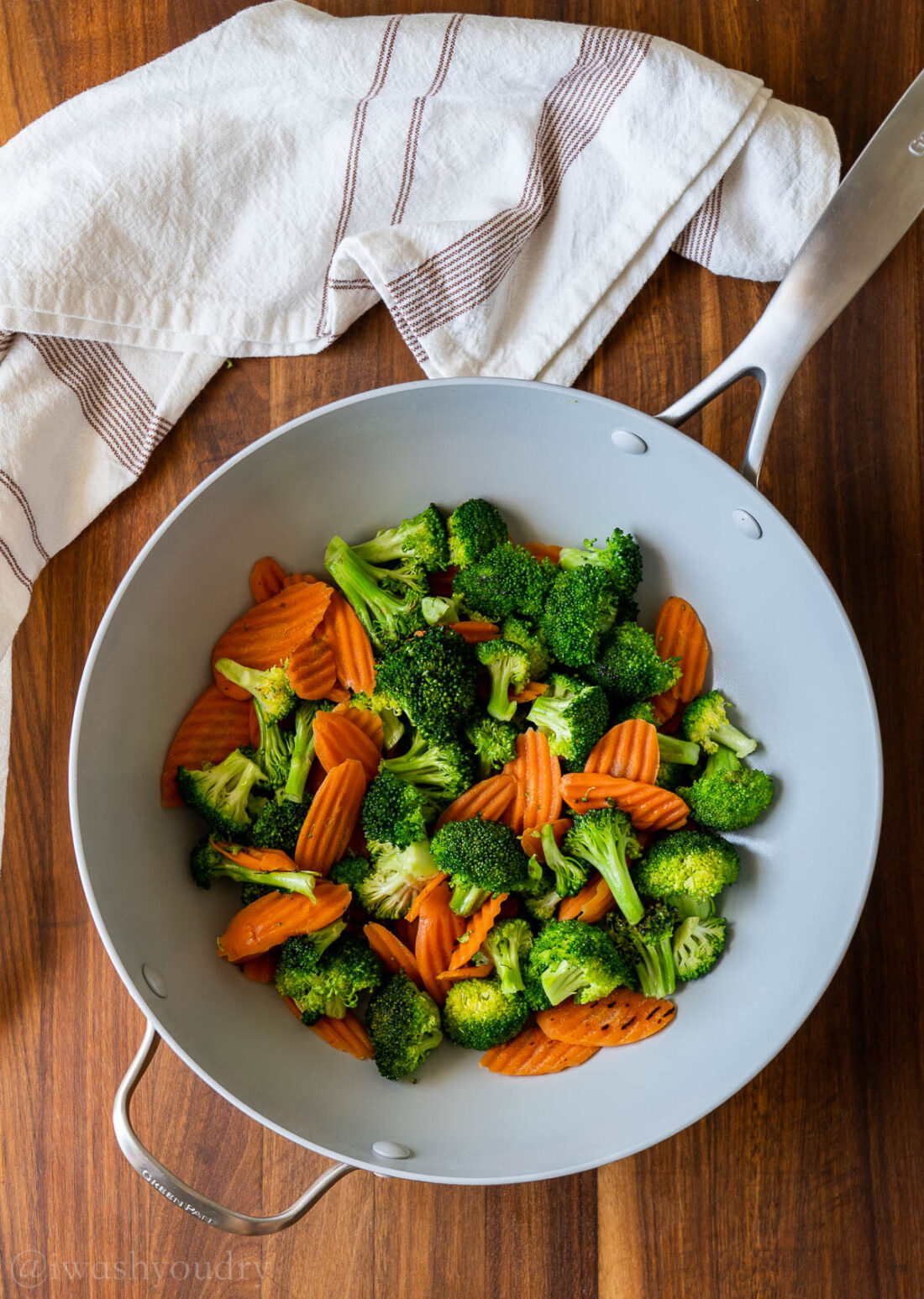 Cooked broccoli and carrots in pan on wood board. 