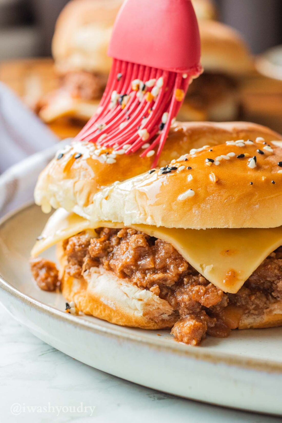 Red pastry brush brushing hamburger bun with sesame seeds and butter.