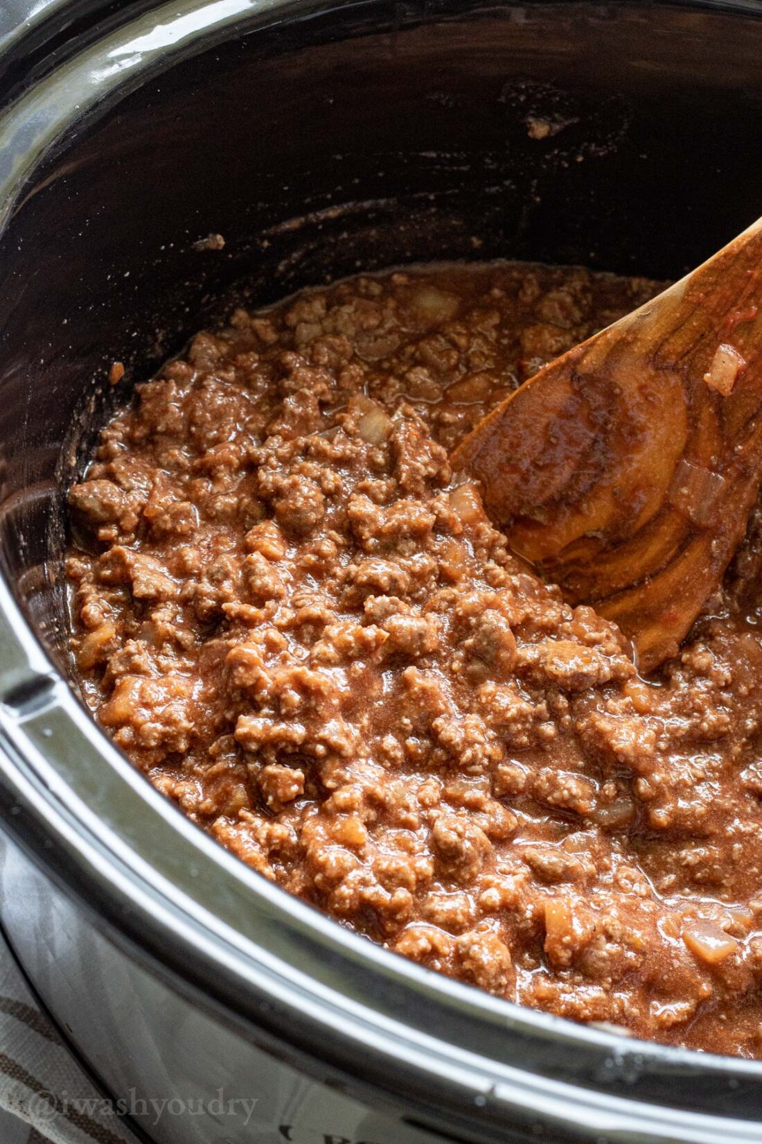 Cooked sloppy joe filling in black crock pot with spoon. 