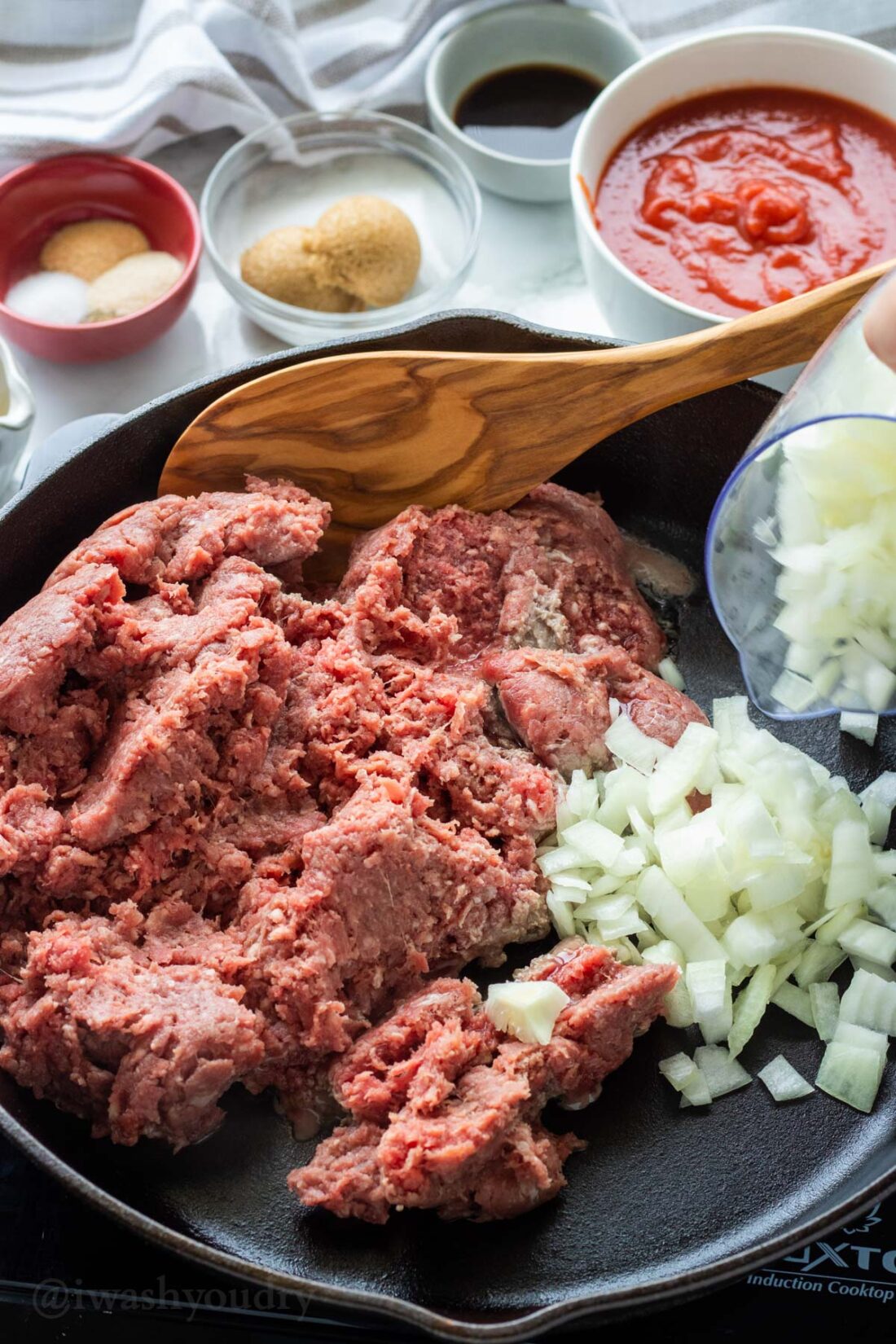 Raw ground beef and onion in cast iron frying pan. 