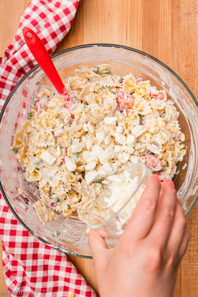 adding feta cheese to bowl of pasta salad