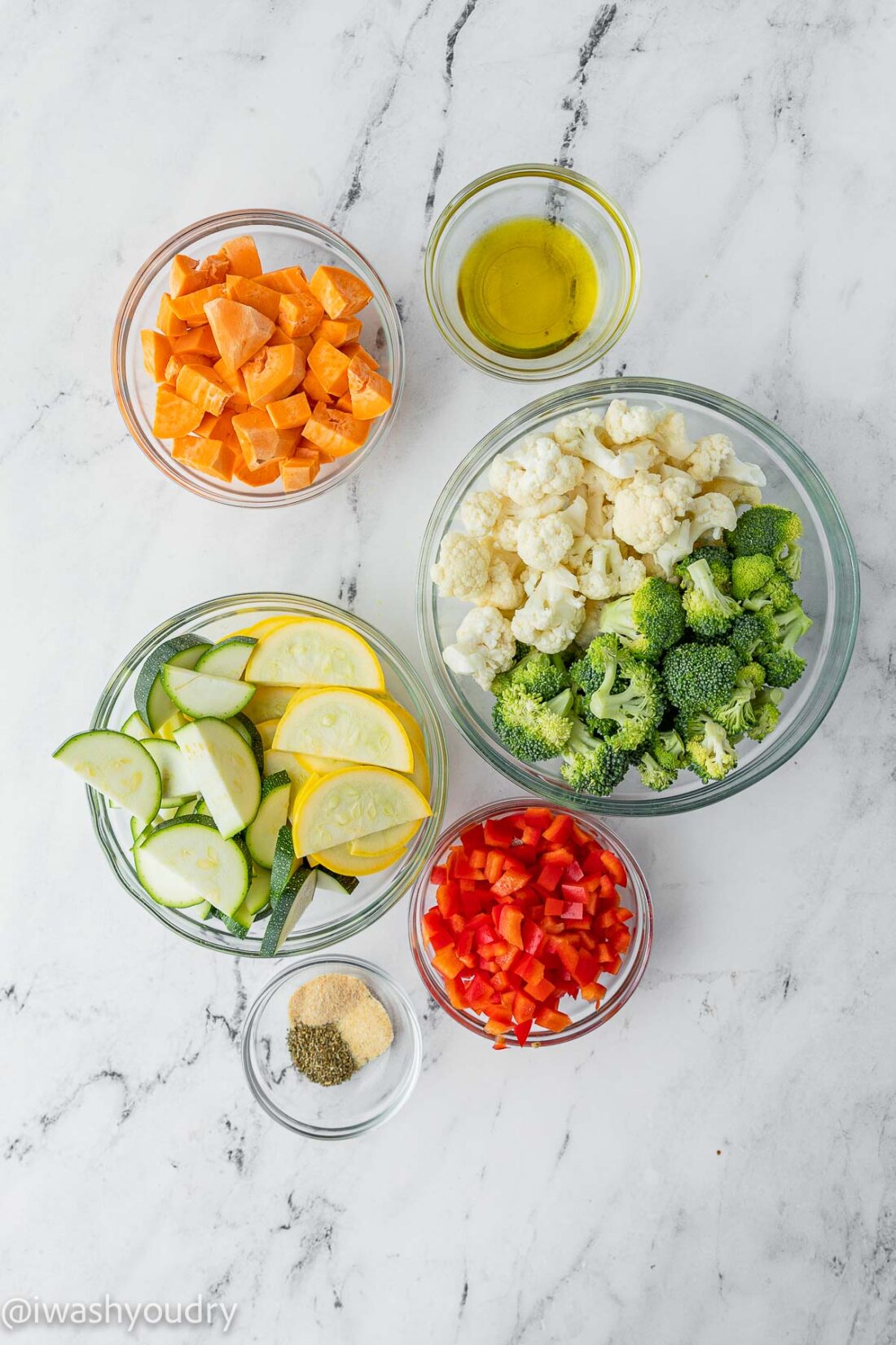 Raw sweet potato, zucchini, squash, cauliflower, broccoli, bell pepper, and spices in glass bowls on marble. 