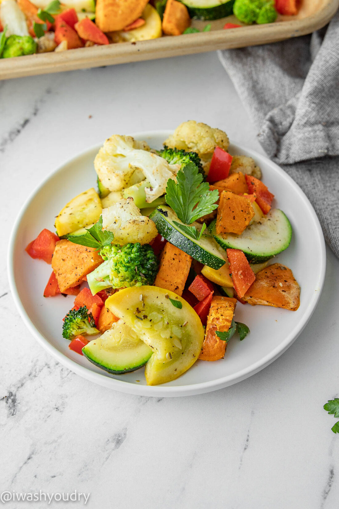 cooked Rainbow Roasted Vegetables on a white plate on marble with dishtowel. 