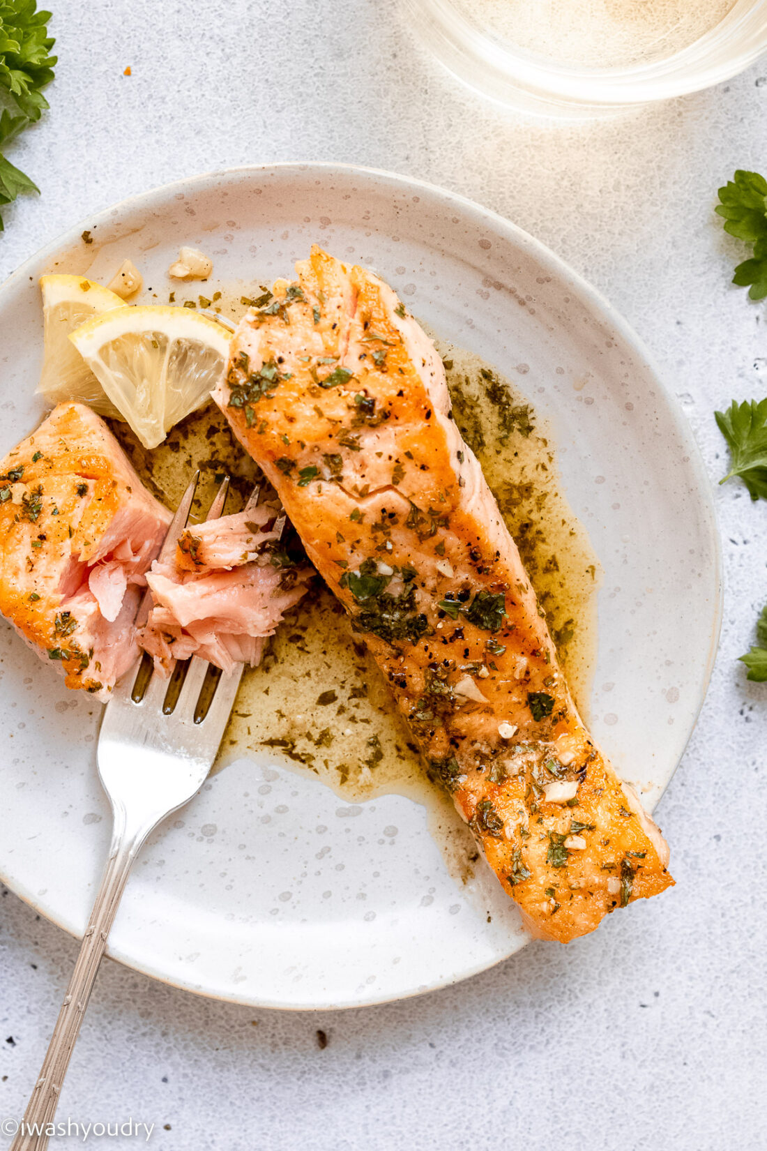 white plate of cooked pan seared lemon garlic salmon with fork and lemon slice. 