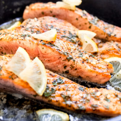 Cooked sliced of salmon in metal pan with lemon slices.