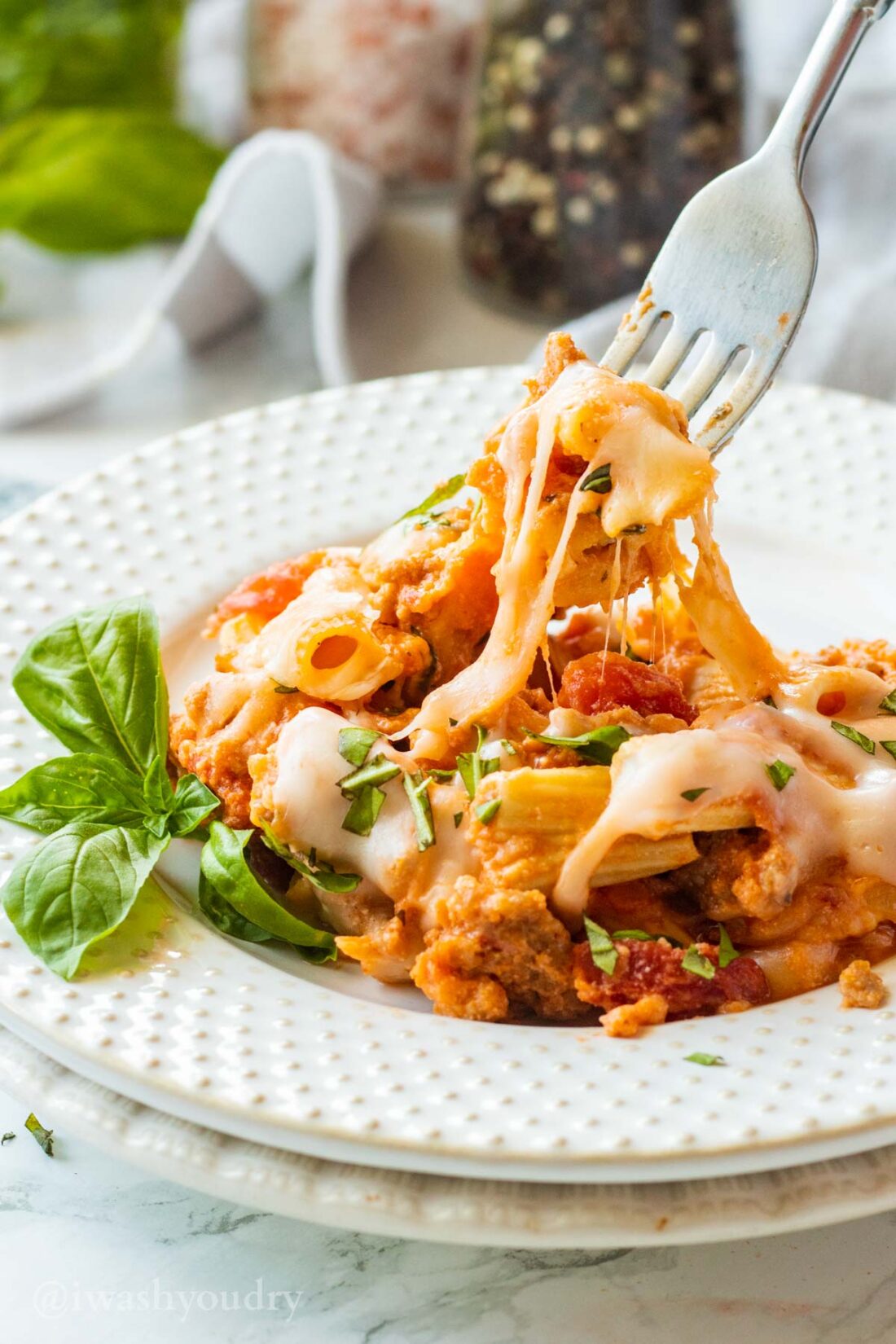 Fork holding up cheesy slow cooker baked ziti above white plate. 