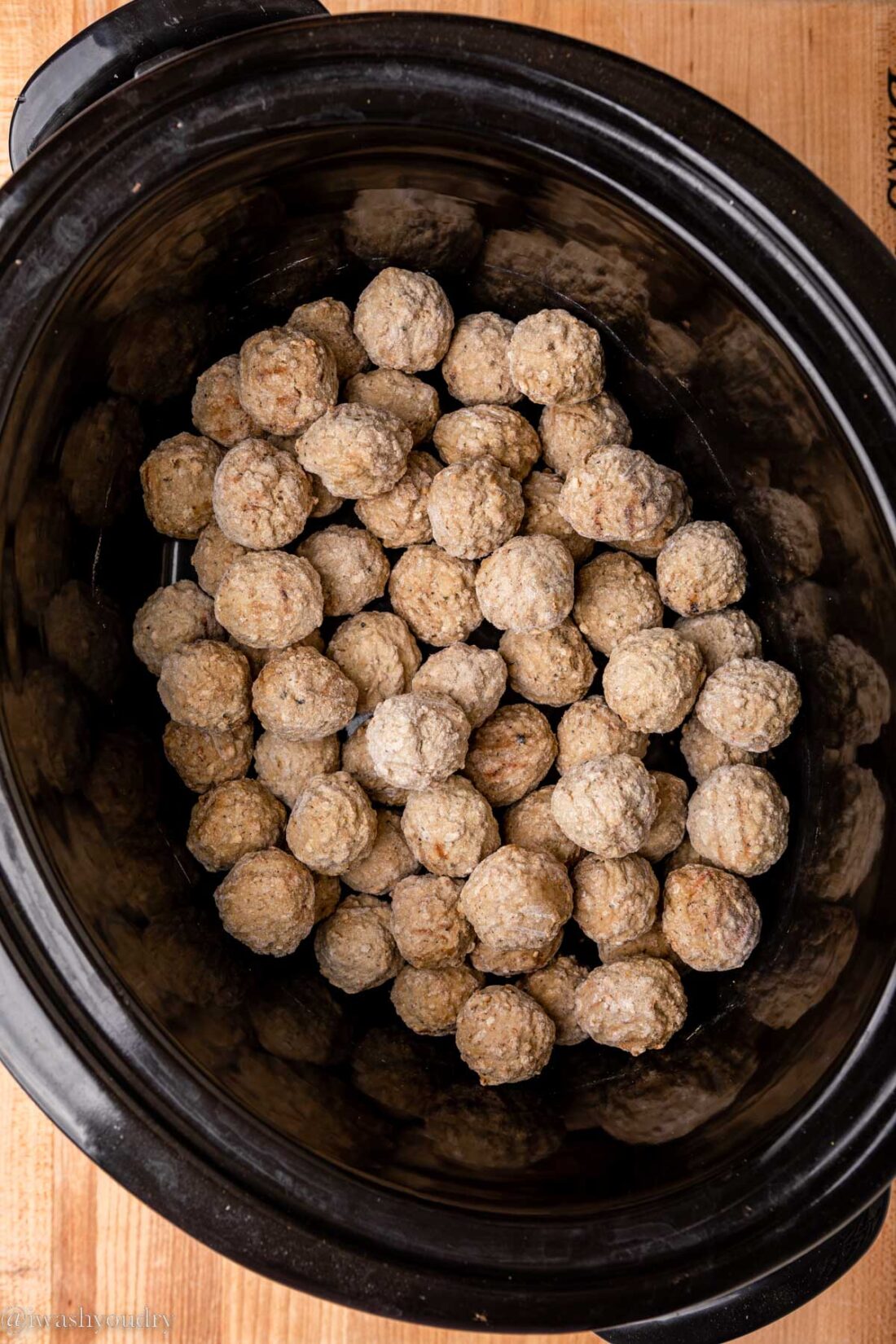 Frozen meatballs in black slow cooker. 