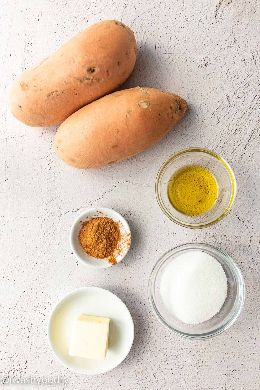 Oil, potatoes, cinnamon, sugar, and butter in dishes on white backdrop. 