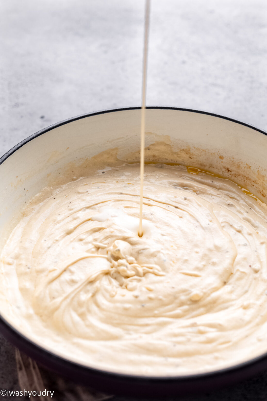 Pouring alfredo sauce into pan.