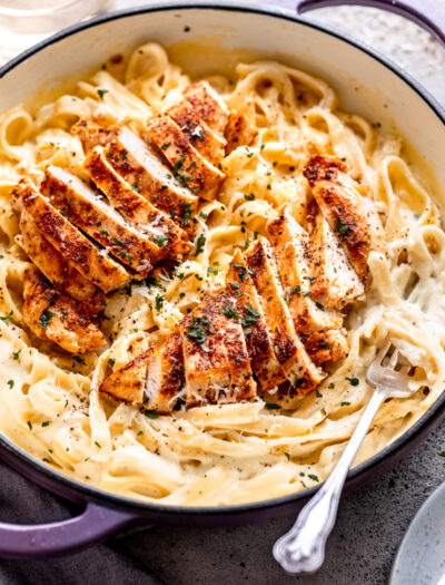 Cooked chicken in pan of noodles and alfredo sauce.