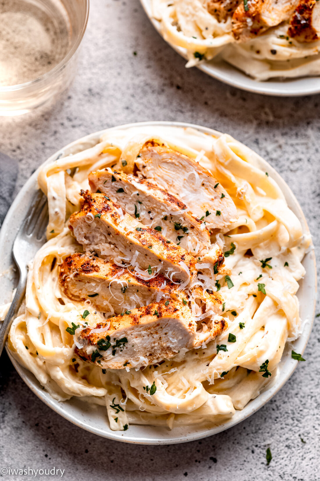 Sliced chicken on white plate of chicken alfredo with fork. 