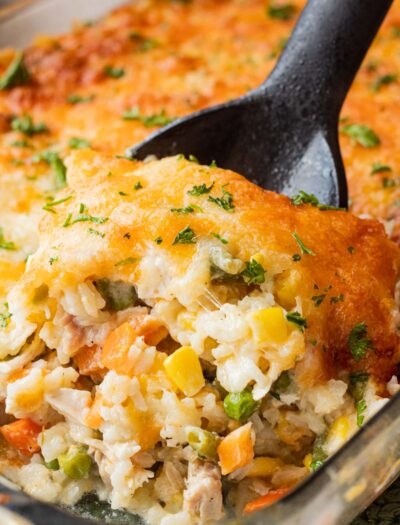 Baked chicken and rice casserole on black spoon in glass pan.