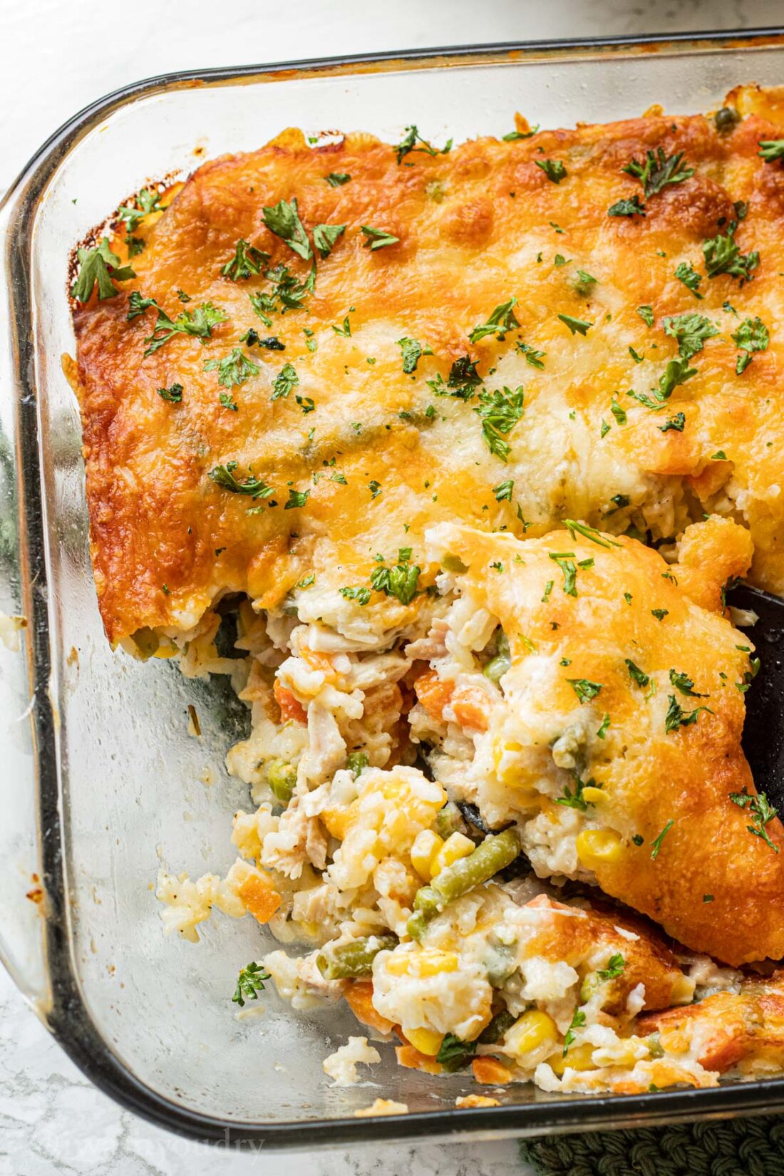 Baked creamy chicken and rice casserole in glass pan with black spoon. 