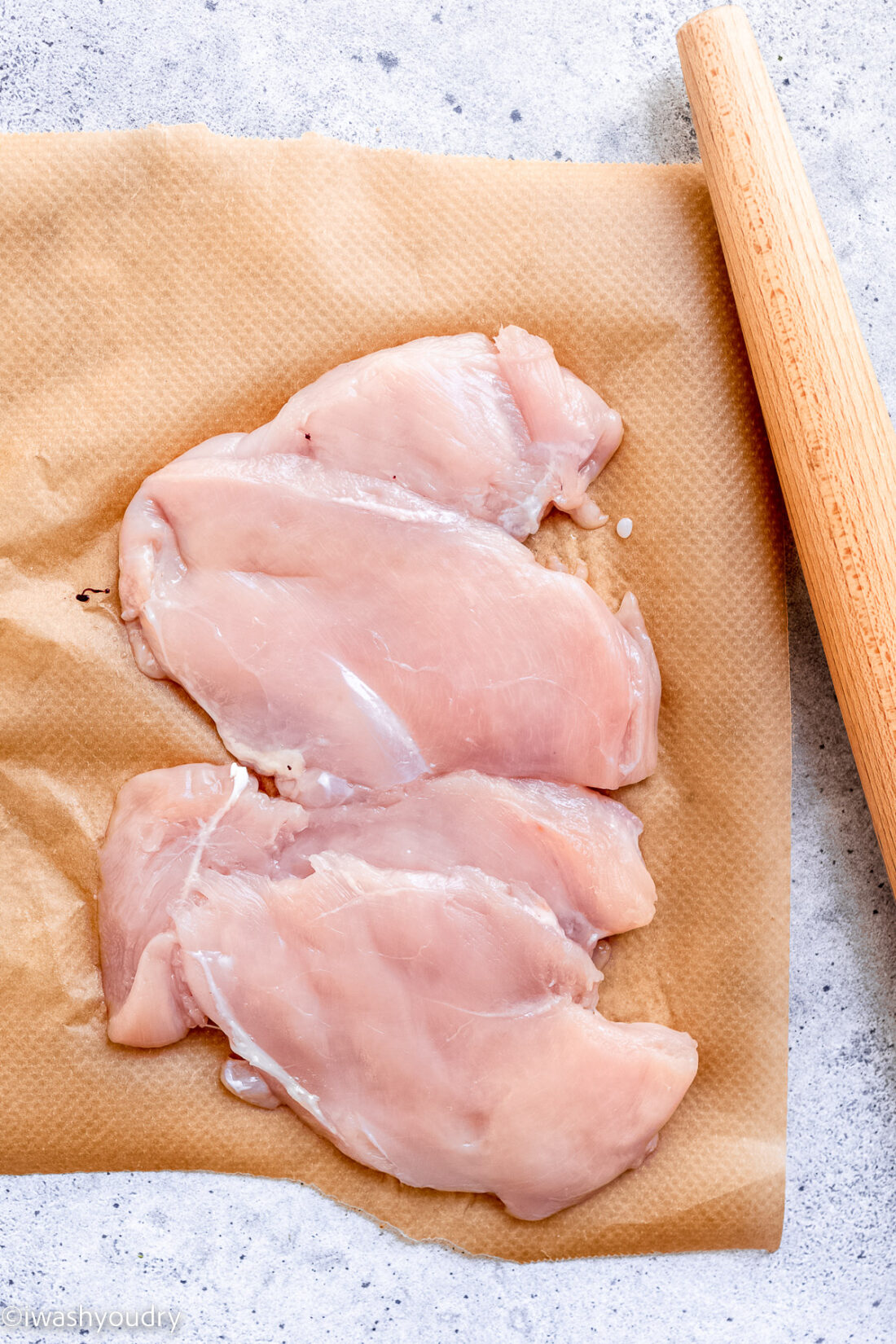 Raw Chicken on brown parchment paper with rolling pin.