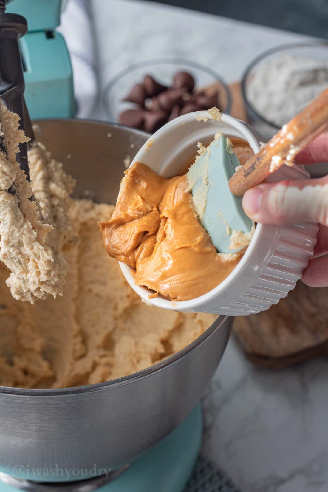 White dish of peanut butter pouring into metal mixing bowl.