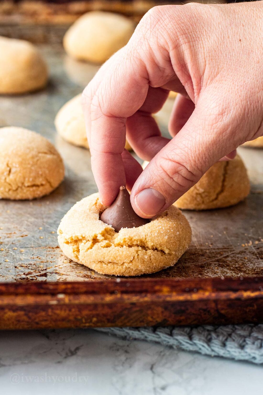 Hand placing chocolate kiss on peanut butter cookie. 