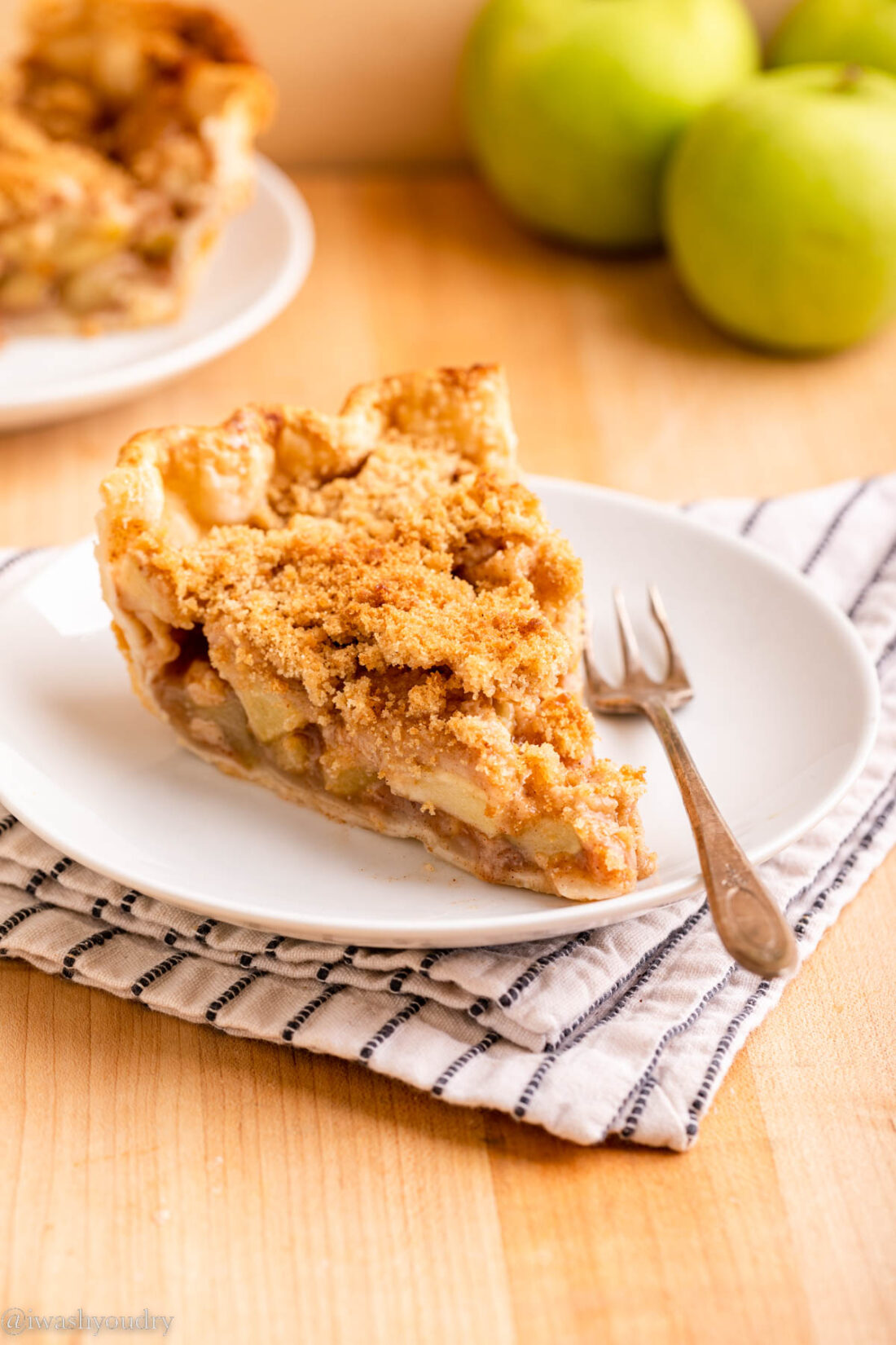 Slice of baked dutch apple pie on white plate with fork on dish towel. 