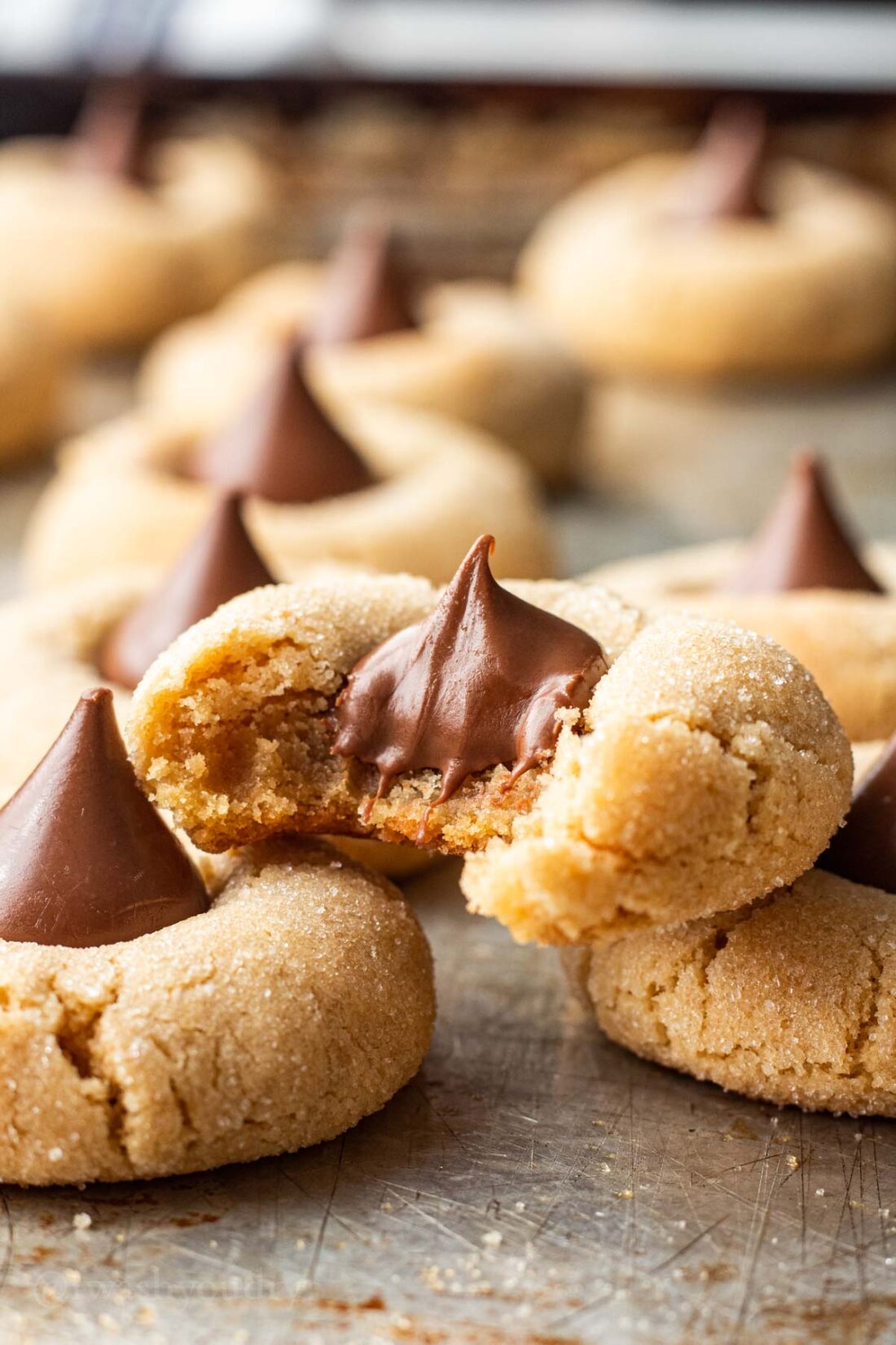 Baked Peanut butter kiss cookie on metal baking sheet with bite taken out. 