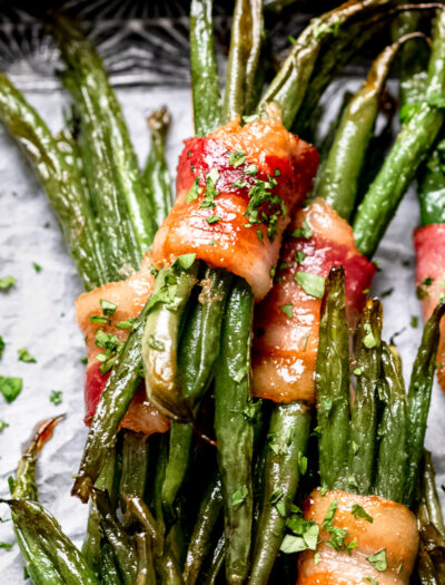 a pile of green beans wrapped in bacon with parsley on top.