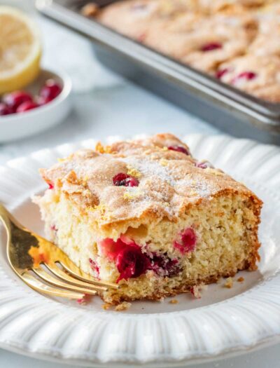 Sliced of baked Cranberry Buttermilk Cake on white plate with gold fork.