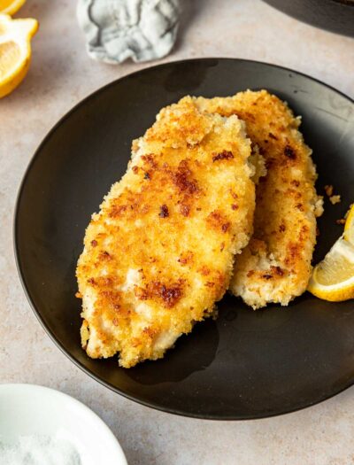 Cooked Chicken Schnitzel on a black plate with lemon wedge.