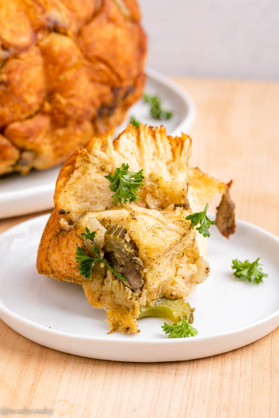 Piece of cooked pull apart stuffing ring on white plate with parsley. 