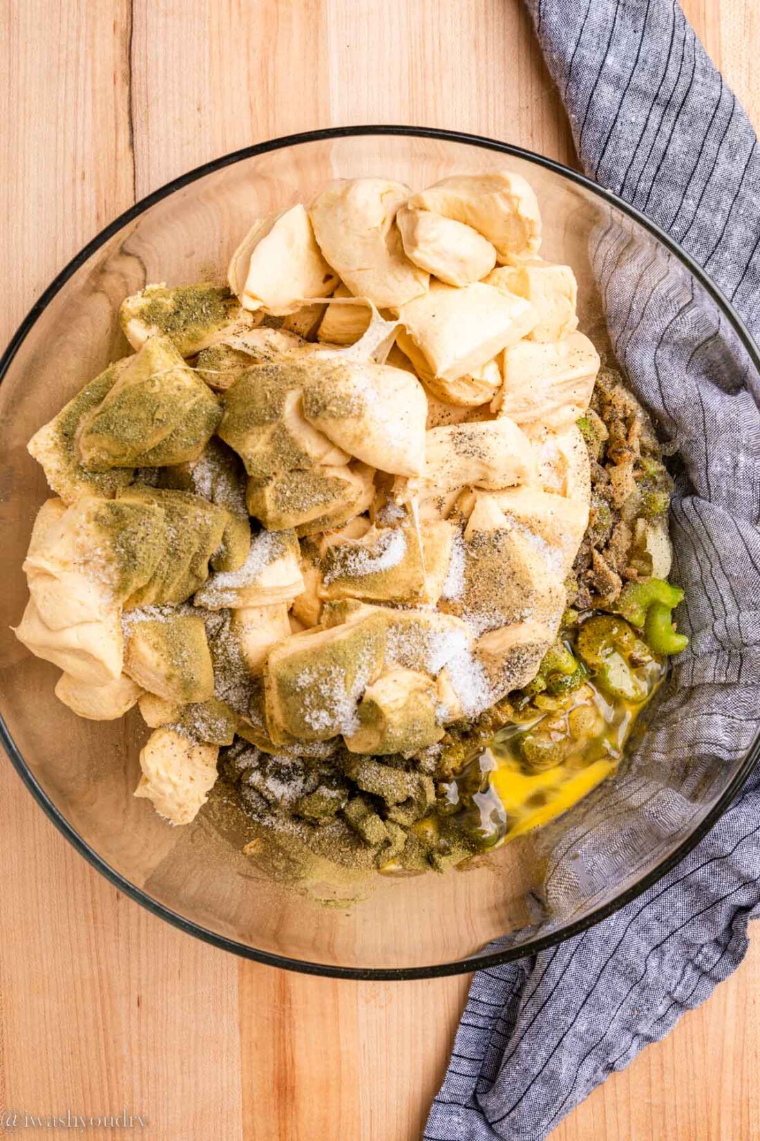 Raw biscuit dough in a glass bowl with spices and cooked vegetables by a blue dish towel. 