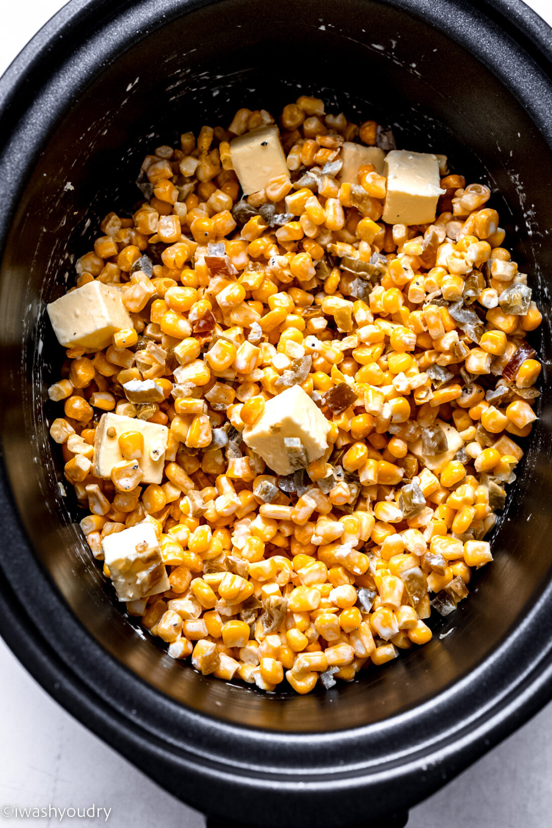 Raw slow cooker creamed corn ingredients in black slow cooker. 