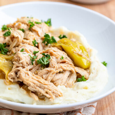 Cookied Slow Cooker Mississippi Chicken on mashed potatoes on white plate.