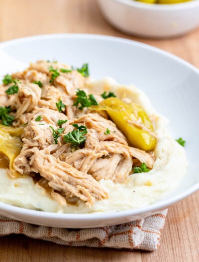 Cookied Slow Cooker Mississippi Chicken on mashed potatoes on white plate.