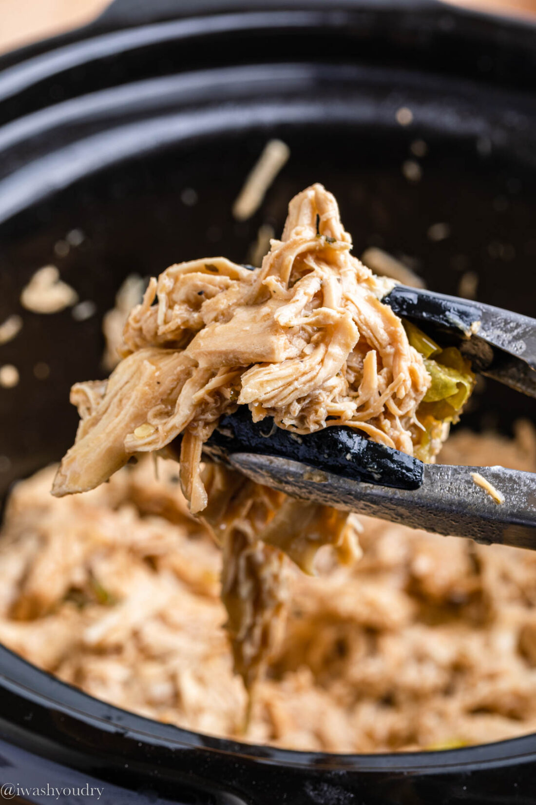 Tongs holding shredded mississippi chicken. 