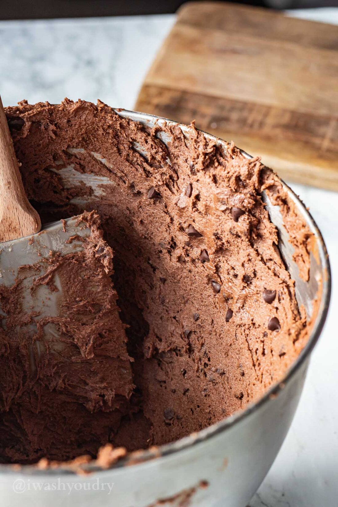 Spatula spreading raw chocolate crinkle dough up the side of a metal bowl. 