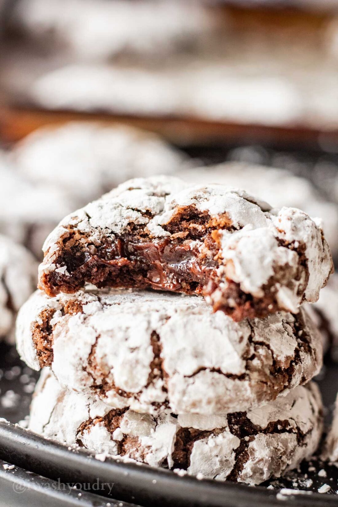 Bite out of baked chocolate crinkle cookie on black plate. 