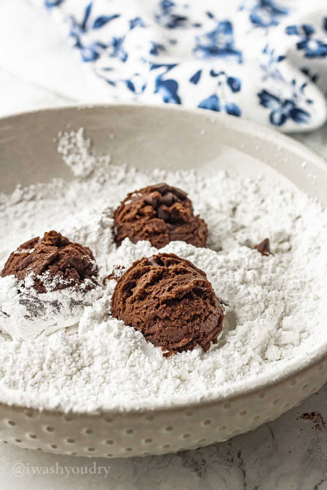 Raw Cookie dough balls in bowl of powdered sugar. 