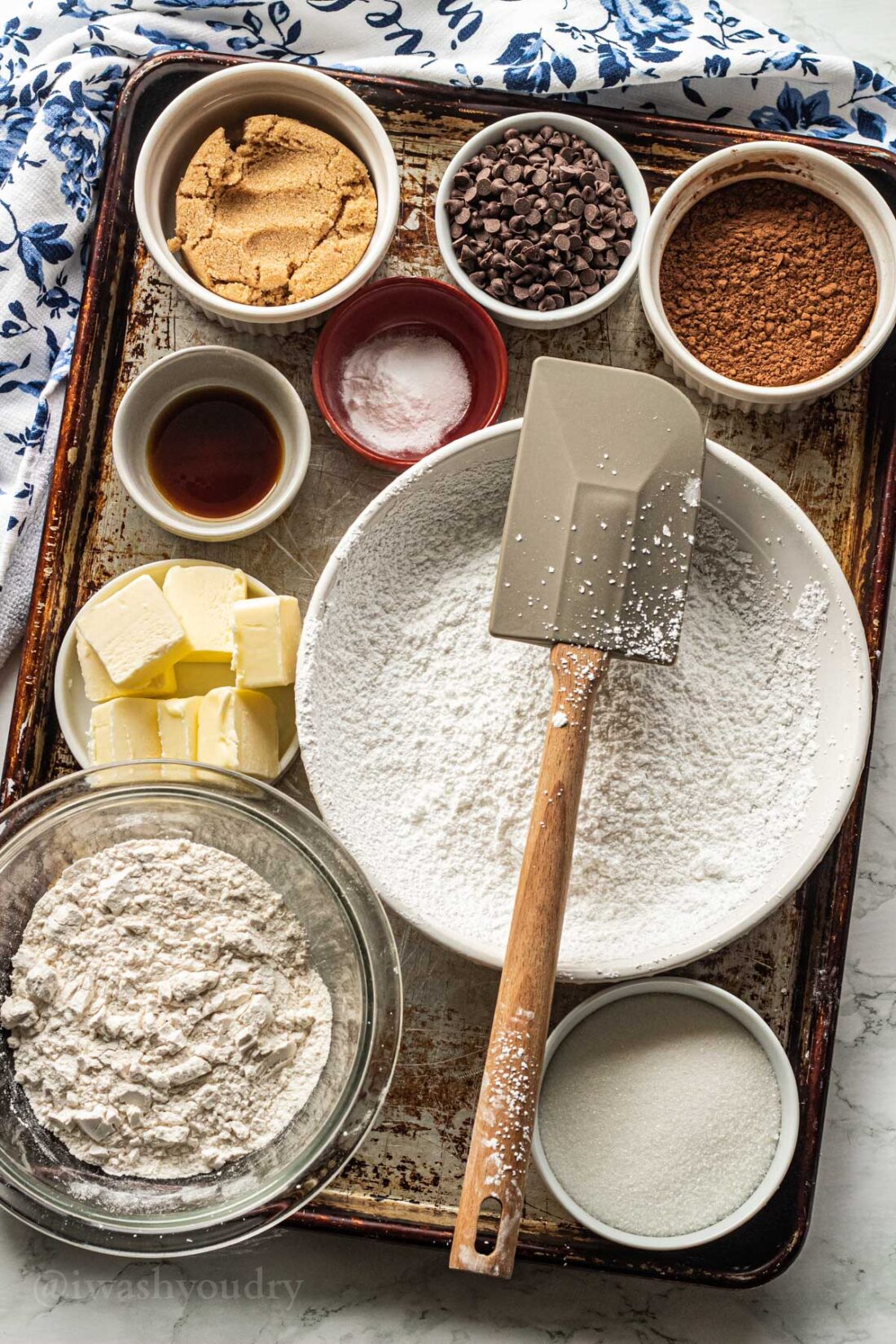 Ingredients for Chocolate crinkle cookies on metal baking pan with blue dishtowel. 