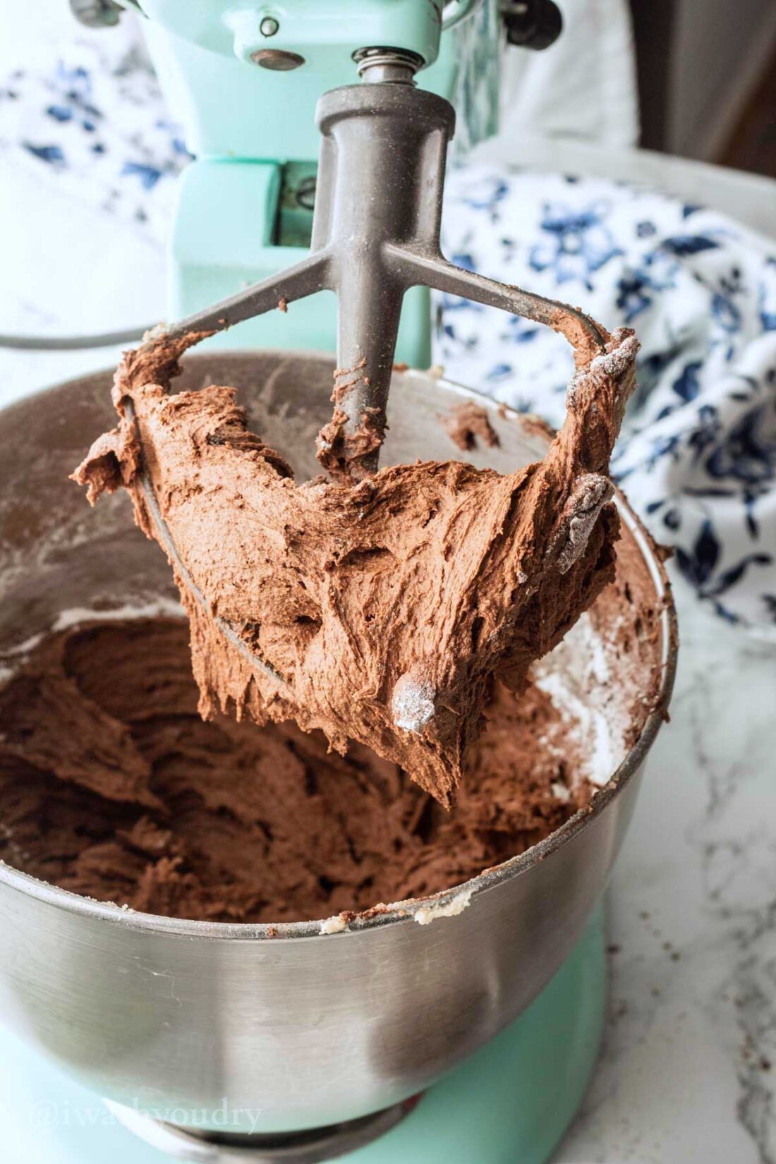 Raw chocolate crinkle dough on metal cookie paddle of blue mixer. 