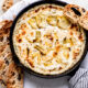 Hot Artichoke Dip in black bowl with slices of bread around.