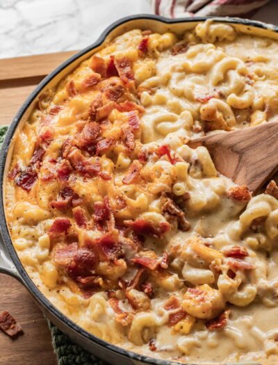 Baked Bacon Mac and Cheese in frying pan with wooden spoon.