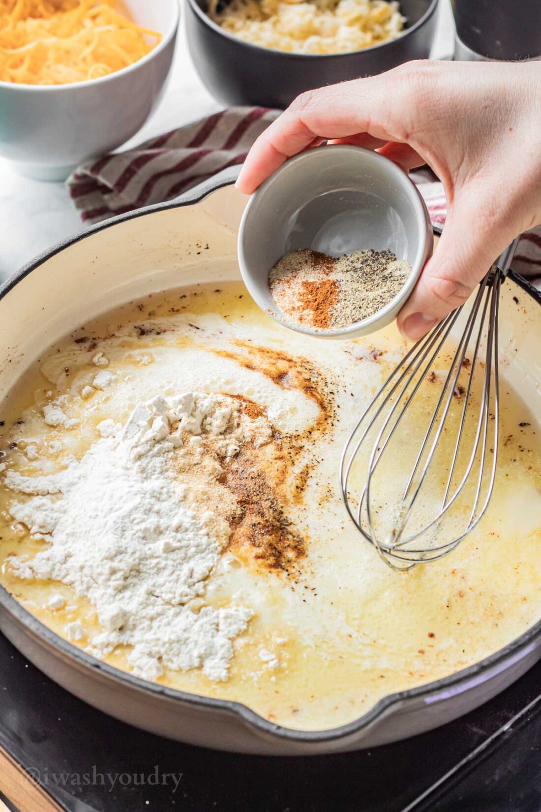 Pouring spices into roux in enameled frying pan. 