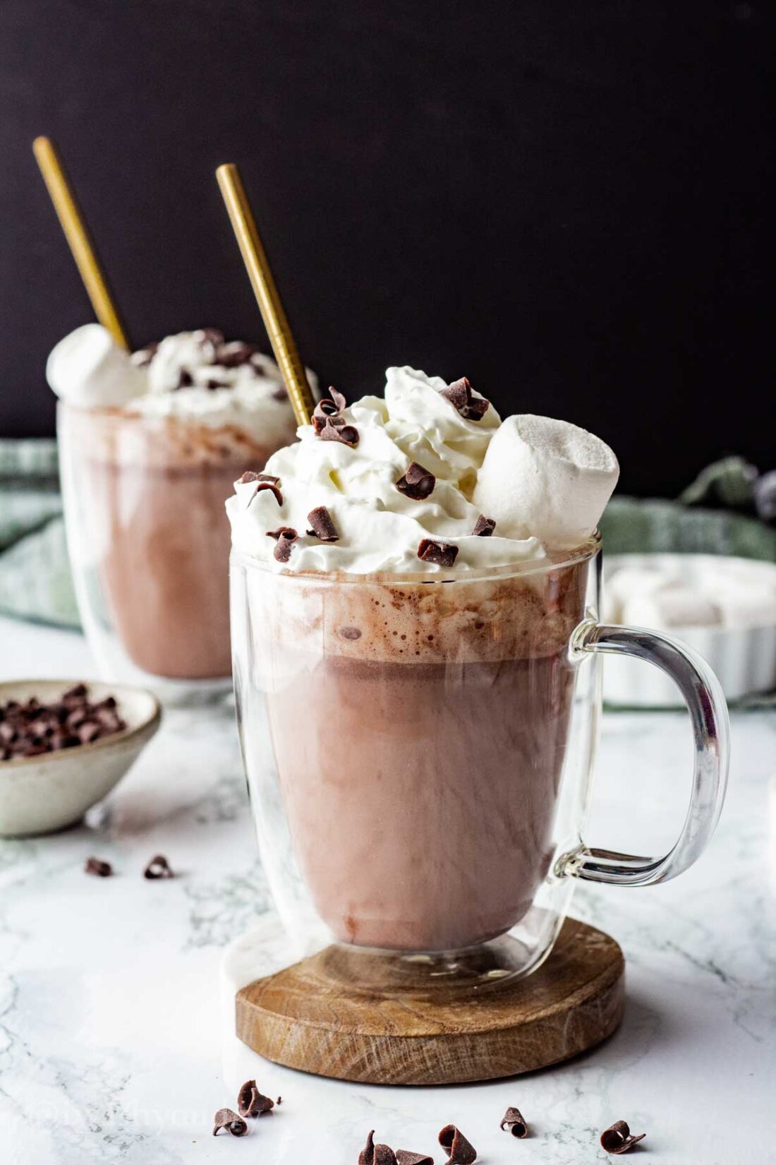 2 mugs of slow cooker hot chocolate with straws on coasters. 