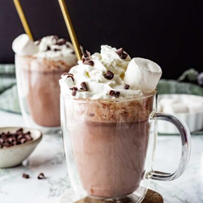 2 mugs of slow cooker hot chocolate with straws on coasters.