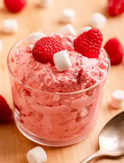 Glass bowl of raspberry fluff salad with spoon on wood table.