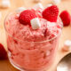 Glass bowl of raspberry fluff salad with spoon on wood table.