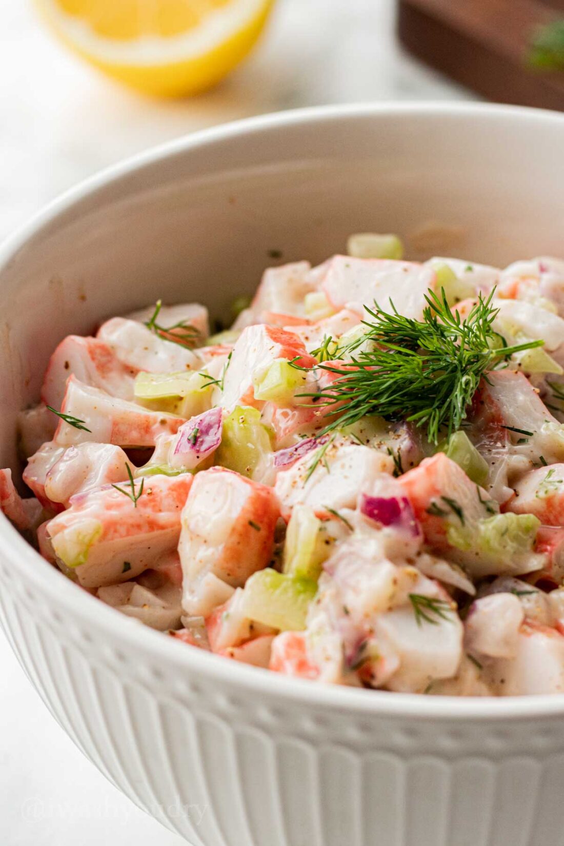 white bowl with creamy crab salad topped with fresh dill weed.